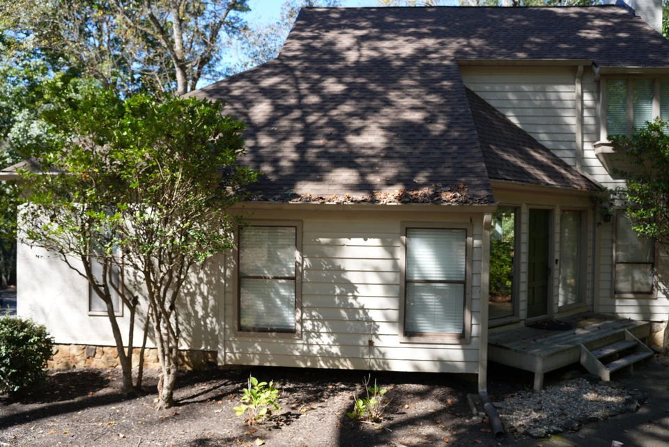 A home's light-sided facade and green front door with trees casting shadows across the roof