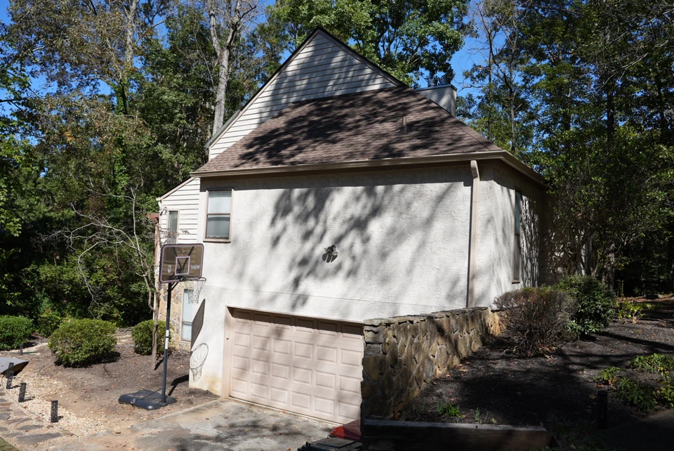 An angled view of a home's garage, stone retaining wall and tree-lined surroundings